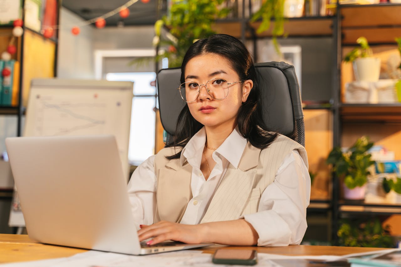 pexels-photo-8278979 Confident businesswoman with glasses focusing on work using a laptop in a modern office setting.